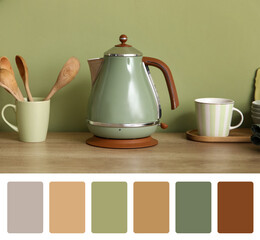 Electric kettle with cup and utensils on table near green wall in kitchen