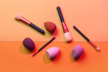 Makeup sponges and brushes on orange background