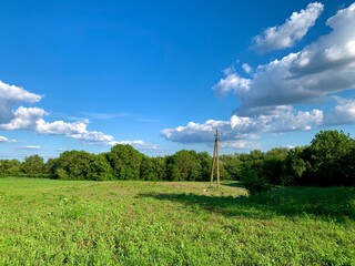 A wide green meadow under a bright blue sky with fluffy white clouds. A single wooden utility pole...