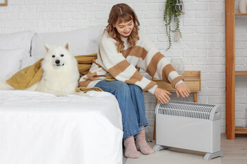 Young woman with blanket and Samoyed dog warming near radiator in bedroom