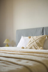 Cozy bedroom interior, beige bedspread and pillow, bedside lamp next to the bed, light from the window