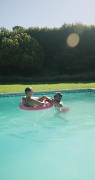 Vertical video: Relaxing in pool, mature couple enjoying sunny morning on inflatable float