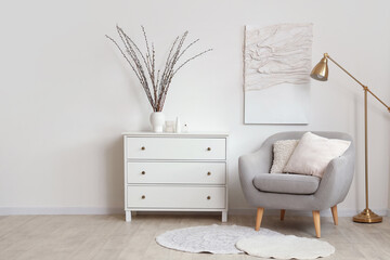 Interior of light living room with armchair, commode and willow branches in vase