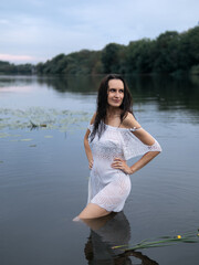 Young beautiful brunette woman in white dress posing in river with water lilies.