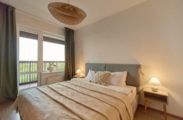 Cozy bedroom interior, beige bedspread and pillow, bedside lamp next to the bed, light from the window