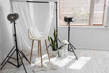 Interior of stylish photo studio with professional equipment, chair, houseplant and rug