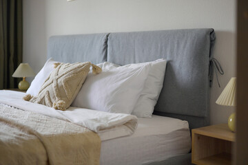 Cozy bedroom interior, beige bedspread and pillow, bedside lamp next to the bed, light from the window