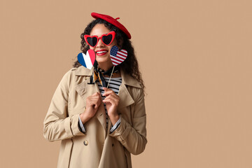 Beautiful young happy African-American woman with USA and France flags in shape of hearts on beige...