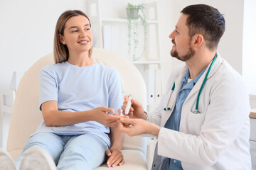 Male endocrinologist measuring blood sugar level of young woman in clinic