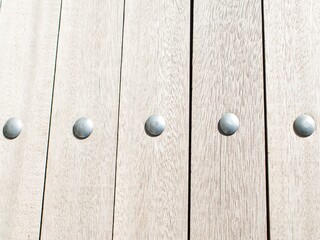 A photo of a close-up of a wooden surface composed of vertical planks. Each plank has a light, almost whitewashed wood grain appearance. Along the middle of the image, evenly spaced across the p