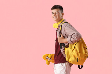 Teenage boy with skateboard and backpack on pink background