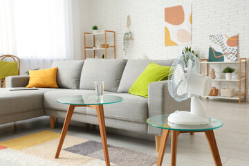 Glass table with modern electric fan near sofa in living room