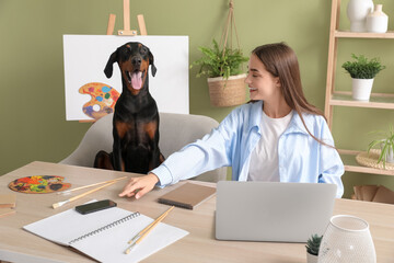 Cute Doberman dog and beautiful young happy woman with paints palettes working at home