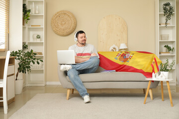 Fototapeta premium Handsome man in headphones with notebook learning Spanish online on sofa at home