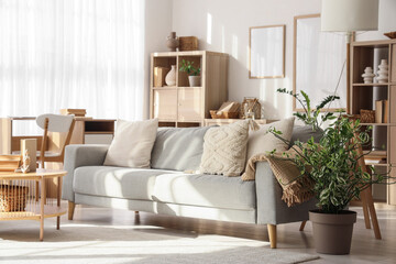 Interior of light living room with sofa, tables and shelf units