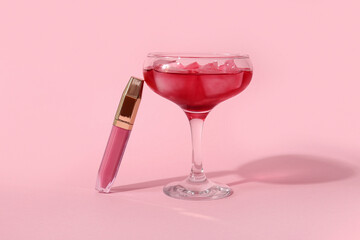 Glass of cocktail and lipstick on pink background