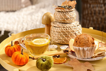 Cup of tea, muffin, burning candles and autumn decor on coffee table in room. Closeup