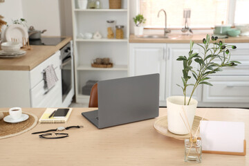 Laptop with mobile phone, wristwatch and coffee cup on dining table in kitchen