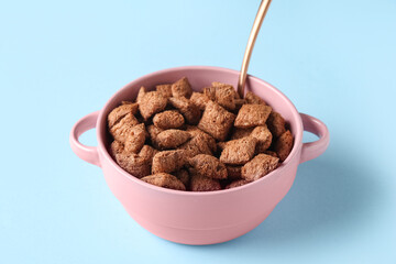 Bowl with tasty chocolate corn pillows on blue background, closeup
