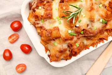 Baking dish with tasty pasta, rosemary, cut green onion and tomatoes on napkin