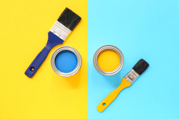 Cans of different paint and brushes on colorful background