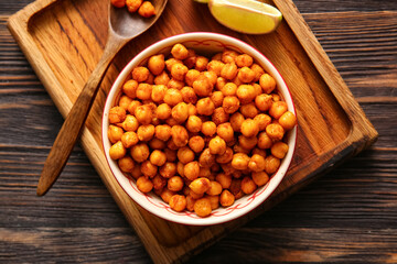 Bowl with tasty fried chickpeas and lime on wooden background