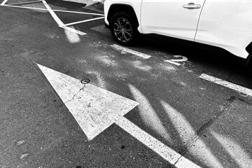 Monochrome image of a portion of a white car and an arrow  road marking.