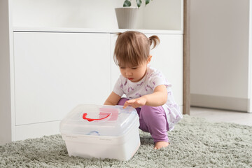 Cute little girl opening first aid kit in kitchen. Child at risk