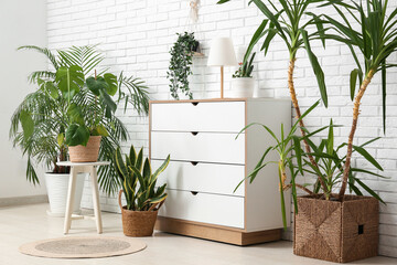 Interior of room with chest of drawers and houseplants near white brick wall