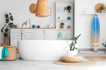 Interior of light bathroom with bathtub, houseplants and surfboard