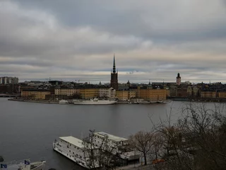 Colorful historic buildings, church spire rising over waterfront, vintage stockholm district capturing nordic maritime scenery under moody clouded skyline