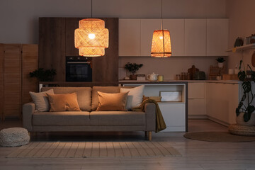 Interior of kitchen with counters, sofa and glowing lamps at night © Pixel-Shot