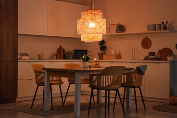 Interior of kitchen with counters, table and glowing lamp at night