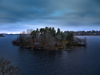 Wooden cabins perched on verdant island, surrounded by calm lake waters, glowing softly under twilight's dramatic gradient sky during peaceful evening hour © Carlos
