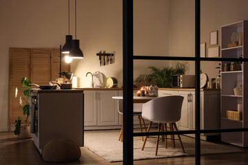 Interior of kitchen with white counters, folding screen and glowing lamps at night