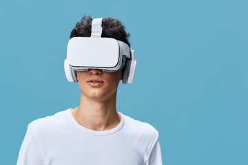 Young man wearing virtual reality headset and white shirt, exploring digital environment against light blue background in modern tech concept.