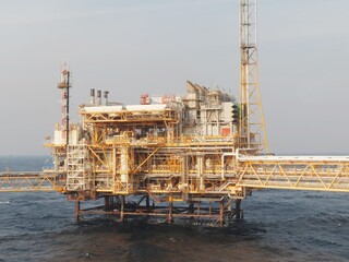Imposing offshore oil platform, a testament to human engineering, stands resilient against the vast oceans relentless waves under a calm, hazy sky. A marvel of industrial design.