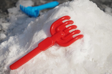 Colorful red plastic toy rake on a snowy surface during winter