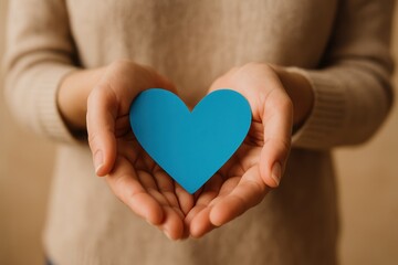 Fototapeta premium Woman s Hands Gently Holding a Blue Paper Heart Against a Softly Focused Background Symbol of Love Care or Charity