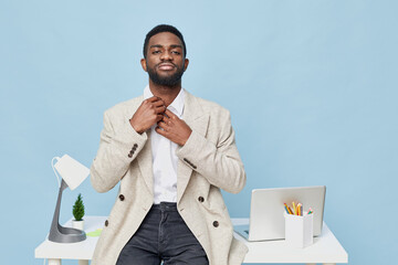 Confident young African American man in beige blazer and white shirt adjusting collar while...