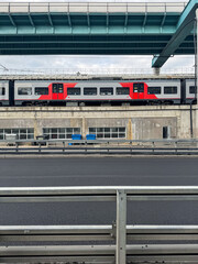 A modern commuter train passes under a highway overpass in an urban environment. Symmetrical lines, concrete textures, and transportation infrastructure create a minimalist cityscape.