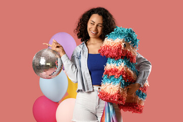 Stylish young African-American woman with disco ball and pinata on pink background
