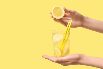 Woman holding glass of fresh lemonade and lemon on yellow background