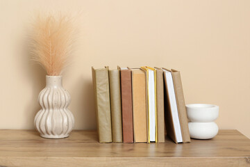 Different books, vase with feathers and decor on wooden table near color wall