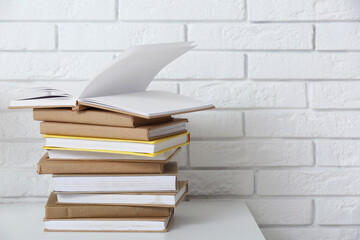 Stack of different books on table near light brick wall