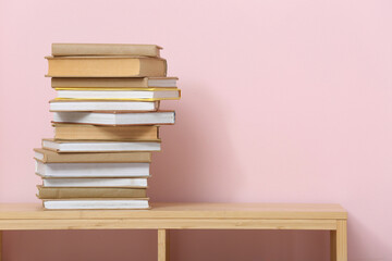 Stack of different books on wooden shelving unit near color wall
