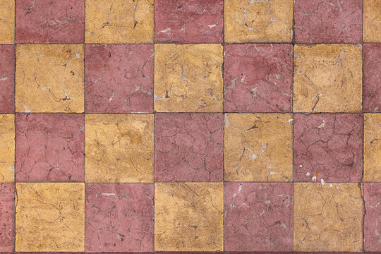 Piso cuadriculado decorado en contraste de amarillo con rojo. Loseta desgastada y vieja. Detalle frontal.