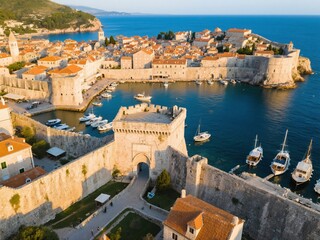 Aerial view of old city walls and towers, the entrance to an ancient stone harbor with boats in the sea at sunset, a bright, sunny summer day in the evening.