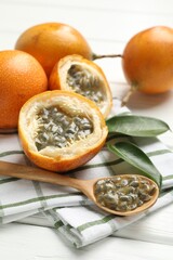 Ripe passion fruits, green leaves and seeds on white wooden table, closeup
