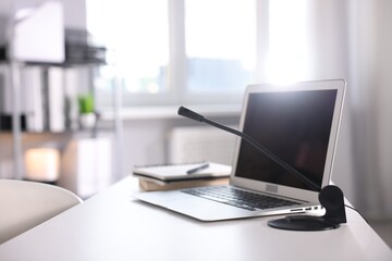 Microphone and laptop on white desk in office. Space for text
